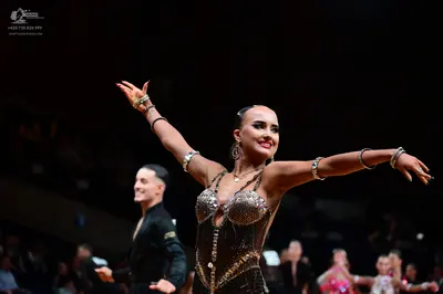 Dancesport competitor: Female dancer: dark, heavily embellished Latin dance bodysuit with bronze/black 