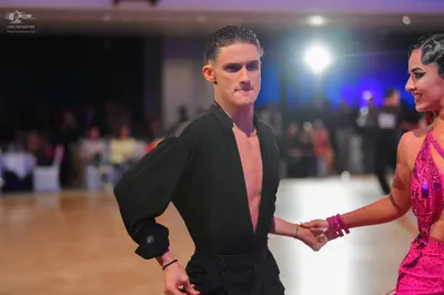 Dancesport competitor: Male dancer: black long-sleeved Latin shirt, unbuttoned at the chest, and black 