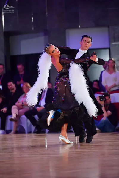 Dancesport competitor: Female dancer: black dress adorned with multicolored sequins and large, volumino
