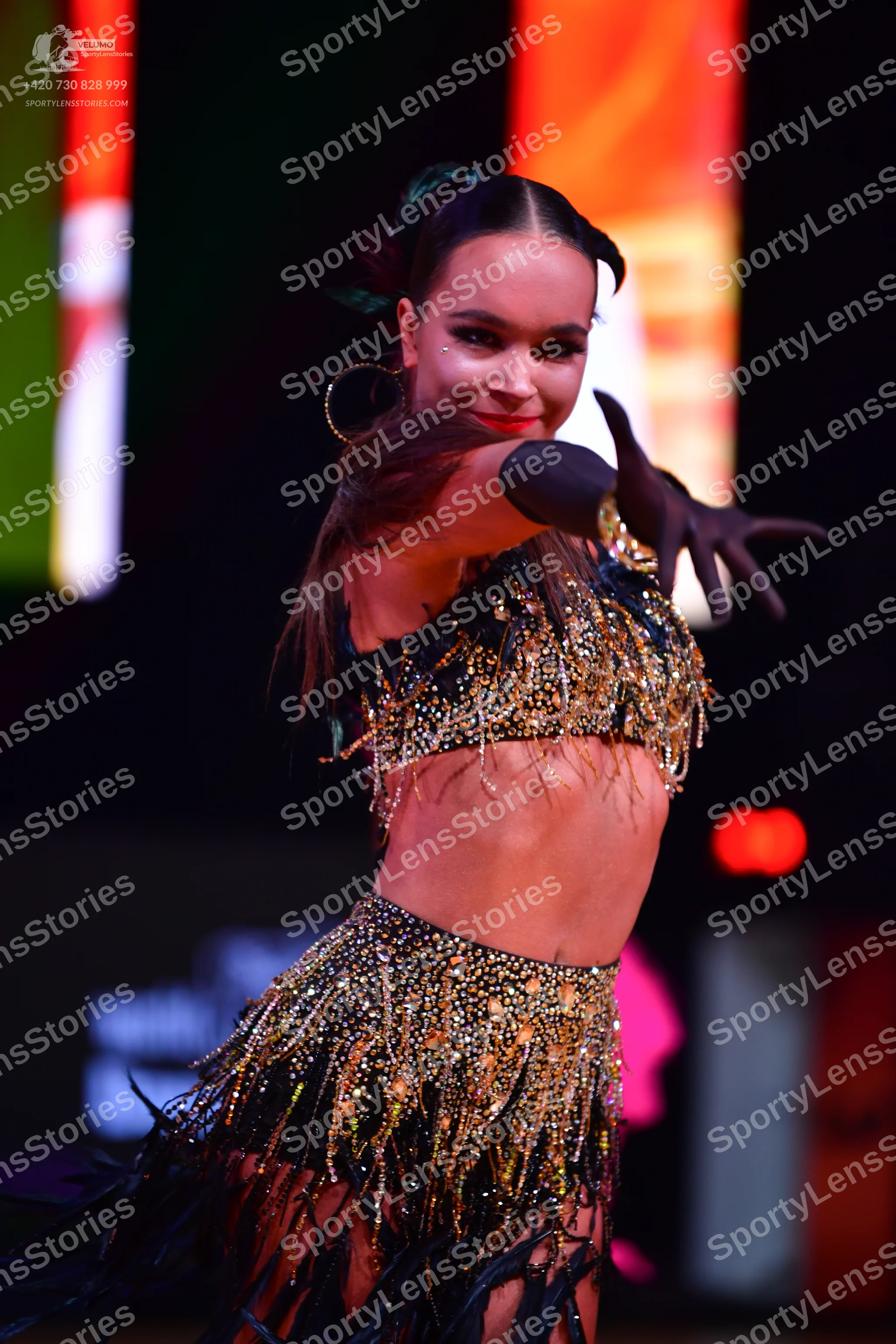 Dancesport competitor: Female dancer: black two-piece Latin costume with gold sequins and fringe, featu