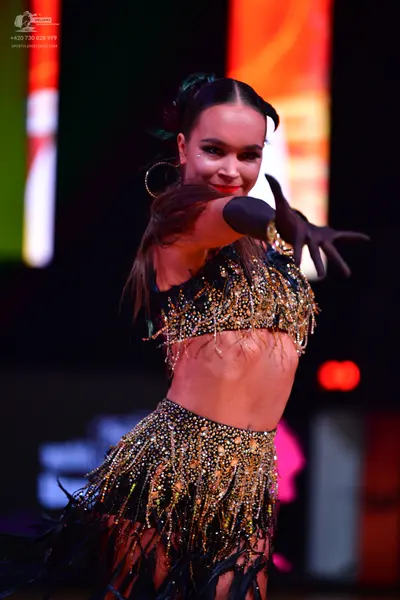 Dancesport competitor: Female dancer: black two-piece Latin costume with gold sequins and fringe, featu