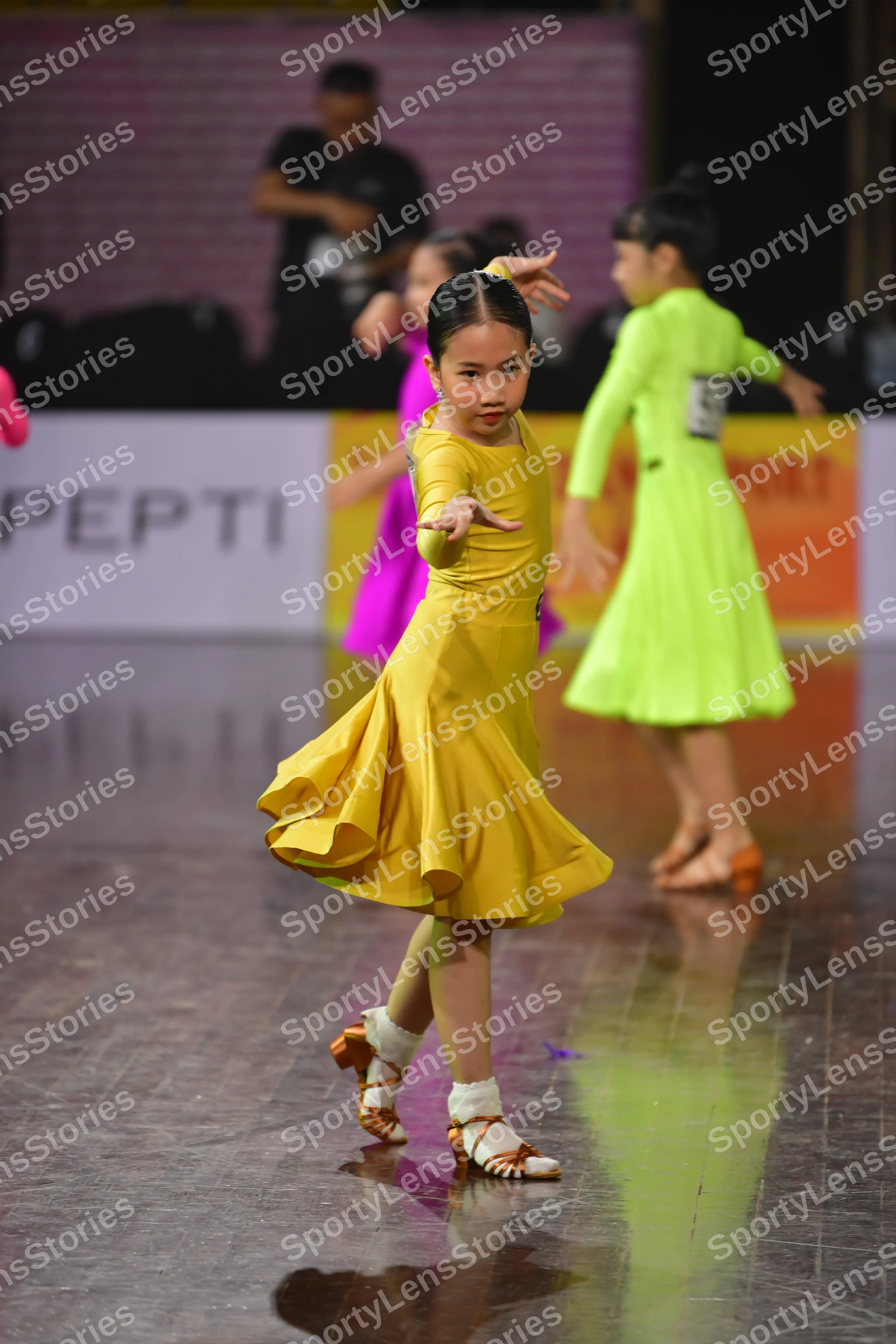 Dancesport competitor #128: Female dancer in foreground: yellow satin latin dress with a flared skirt and go