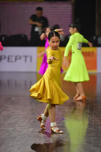 Dancesport competitor #128: Female dancer in foreground: yellow satin latin dress with a flared skirt and go
