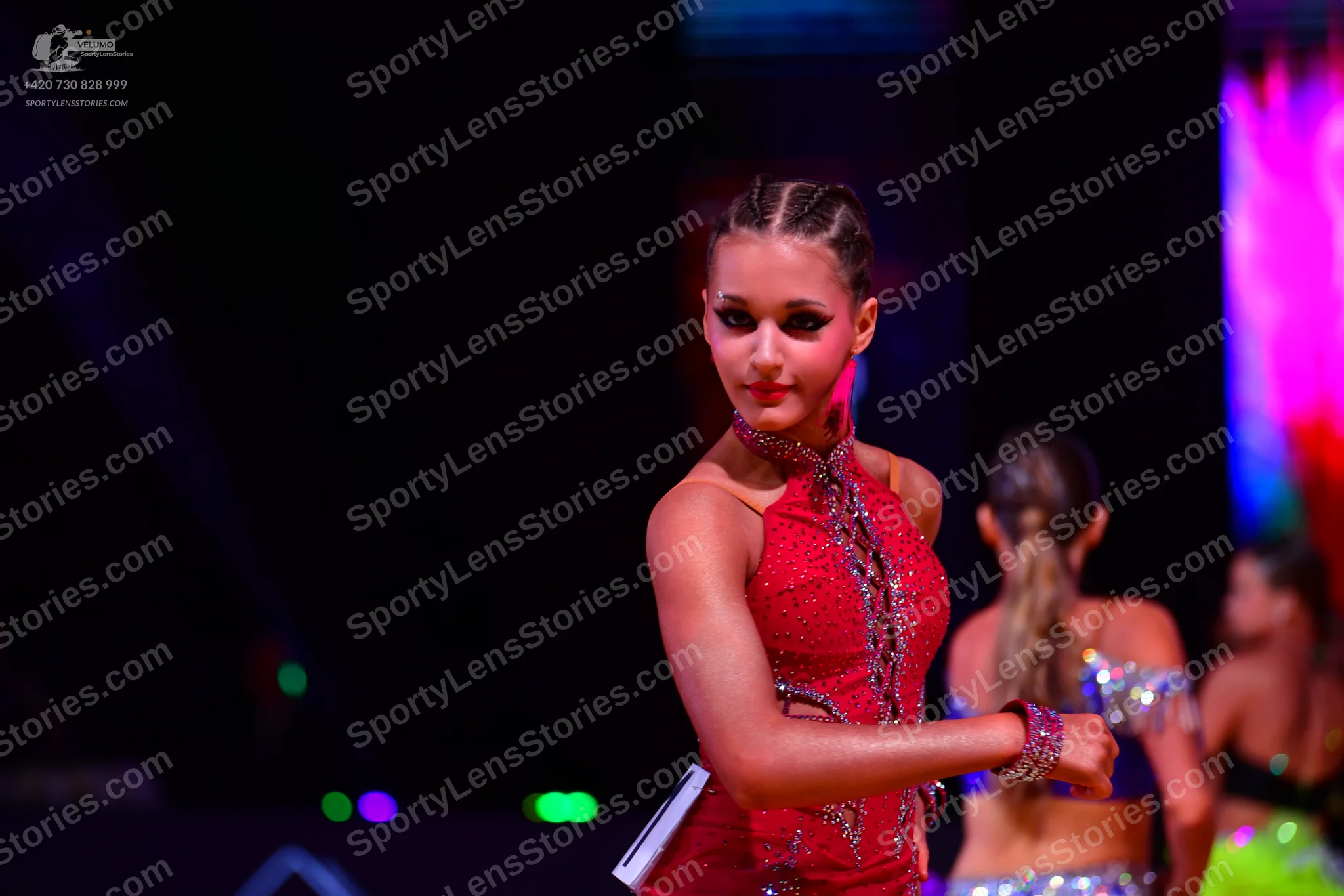 Dancesport competitor: Female dancer in foreground: red latin dress with red sequins and a high neck