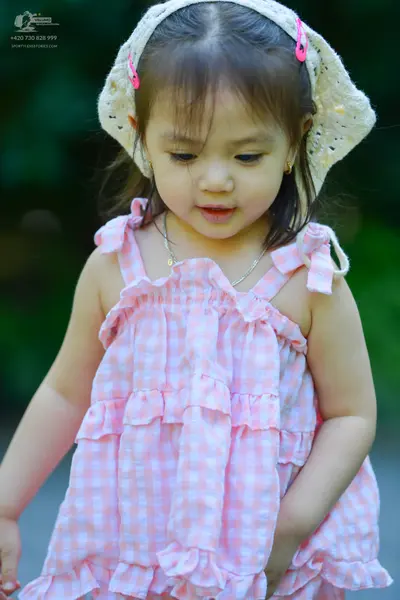 Dancesport competitor: The child is wearing a pink and white gingham patterned sleeveless dress with ru