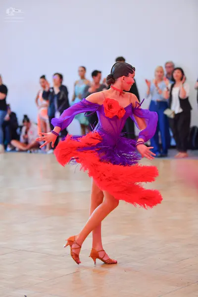 Dancesport competitor: Female dancer: purple latin dress with sheer sleeves, a large red rose on the bo