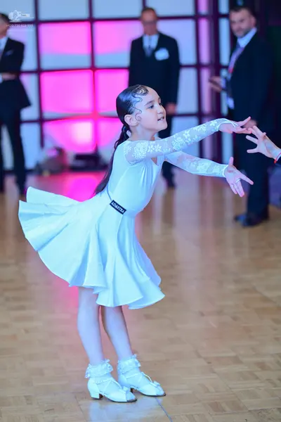 Dancesport competitor: Female dancer: white latin dress with long lace sleeves and a flared skirt, and 