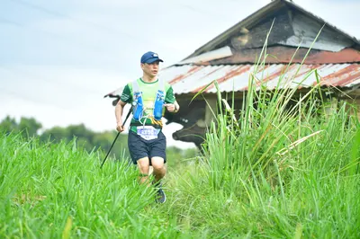 Marathon runner #3115: Runner 1: light green sleeveless shirt, blue and white hydration vest, black sho