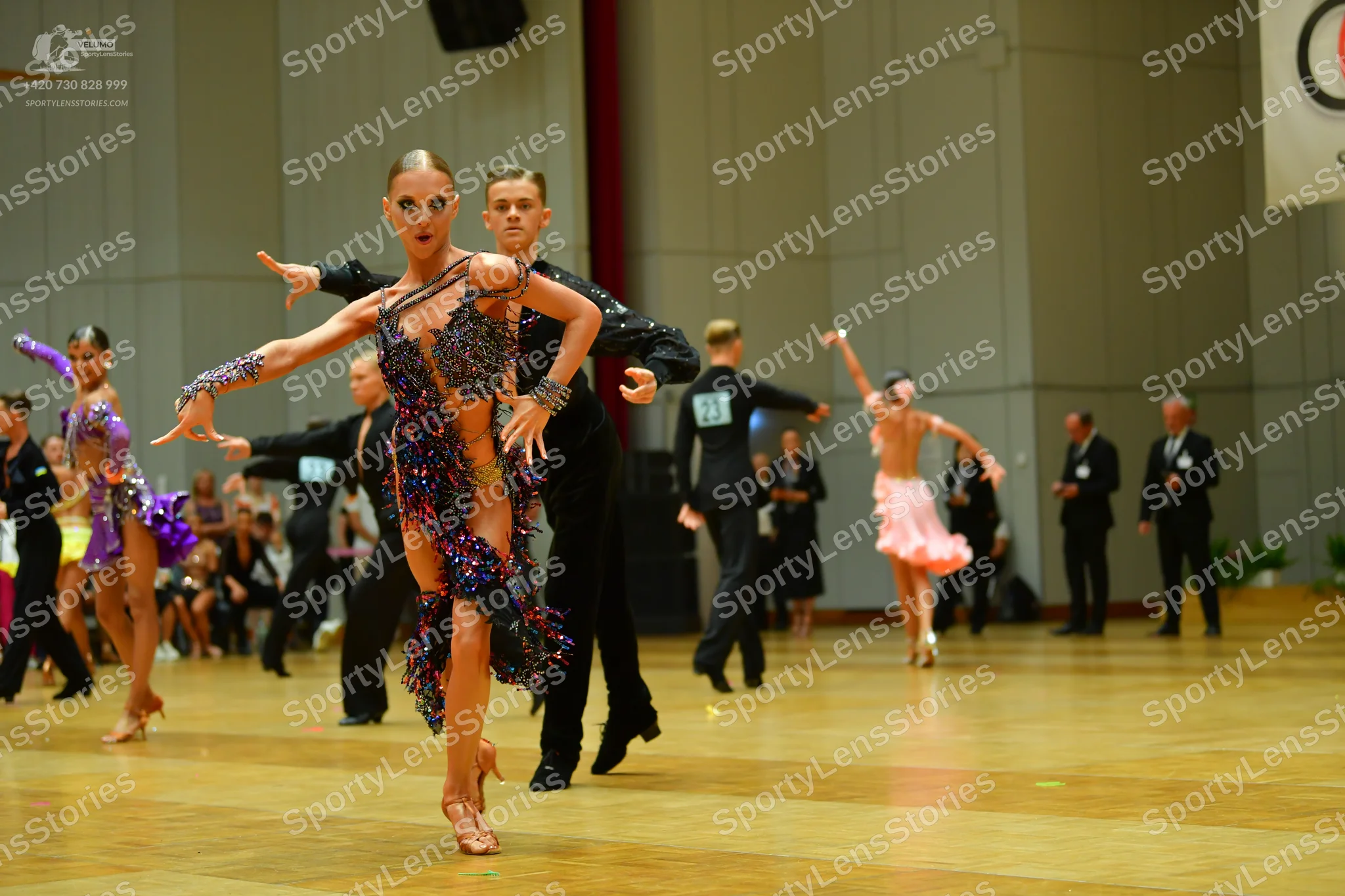 Dancesport competitor: Foreground female dancer: multi-colored sequined latin dress with brown, purple,