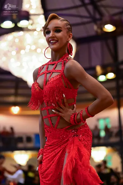 Dancesport competitor: Female dancer: red latin dress with sequins, fringe, and cutout details, accompa