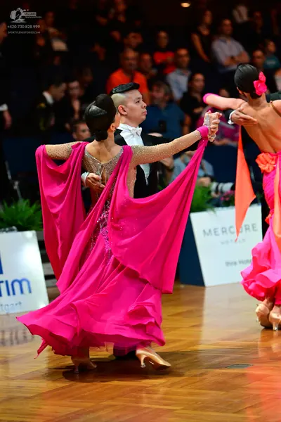 Dancesport competitor: Female dancer: pink ballgown with a large, flowing skirt and sheer sleeves with 