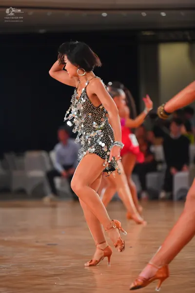 Dancesport competitor: Female dancer in foreground: black Latin-style dress/leotard heavily embellished
