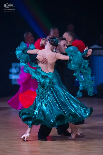 Dancesport competitor: Female dancer (foreground): teal ballroom dress with voluminous, ruffled layers 