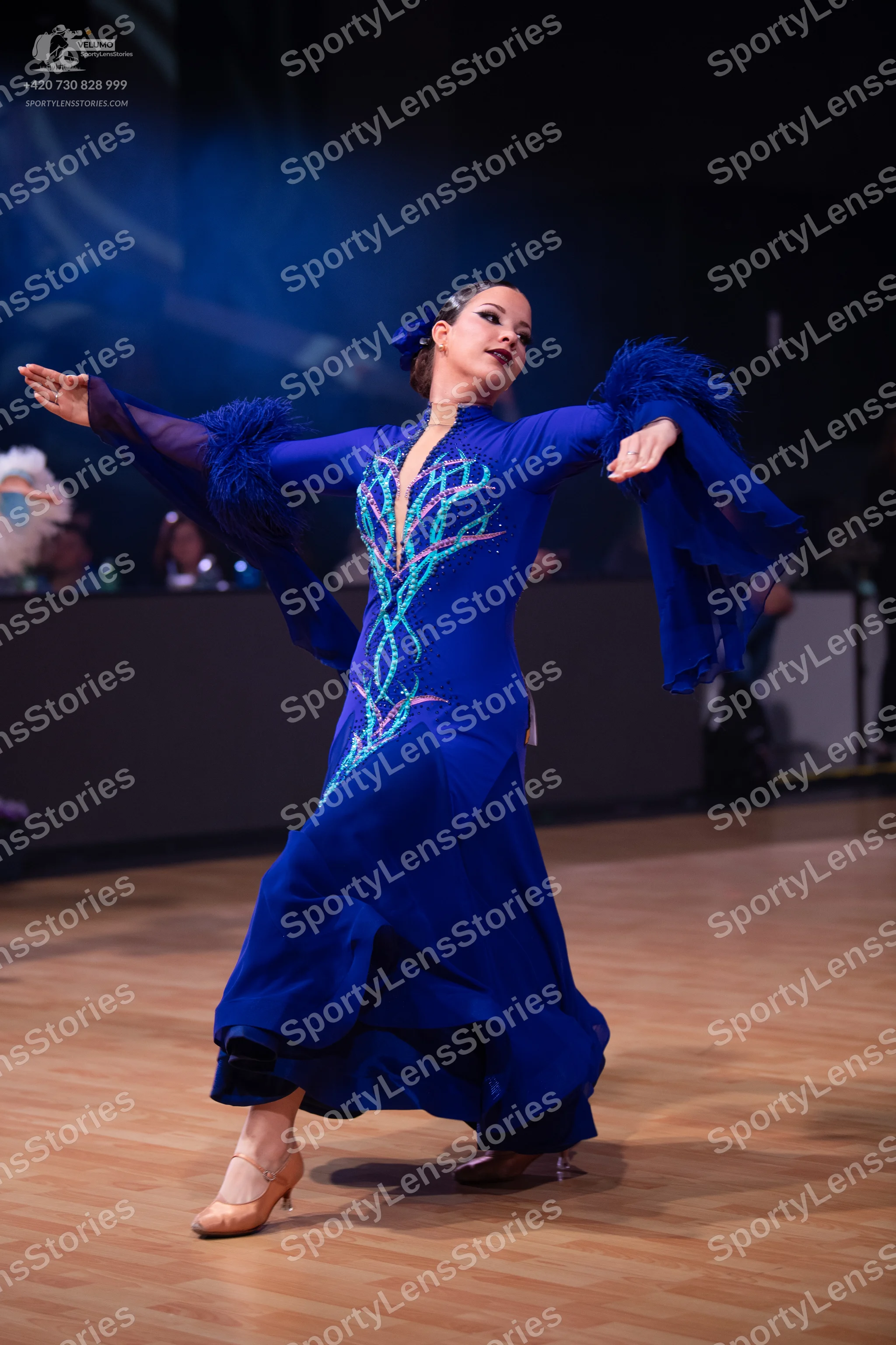 Dancesport competitor: Female dancer: royal blue ballroom gown with long, flared sleeves featuring text