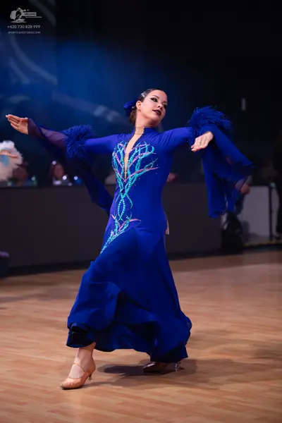 Dancesport competitor: Female dancer: royal blue ballroom gown with long, flared sleeves featuring text