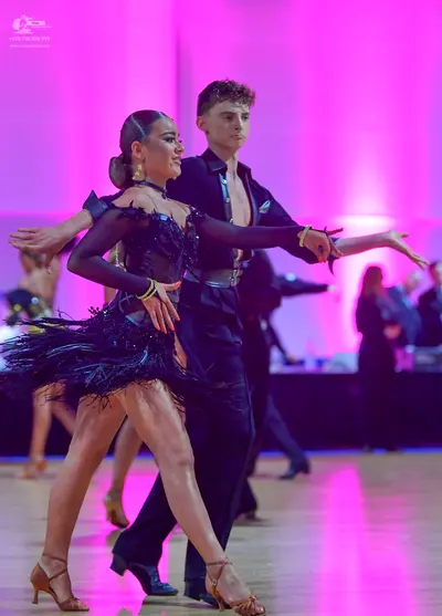 Dancesport competitor: Female dancer: black latin dress with long sheer sleeves, feathered/fringed skir