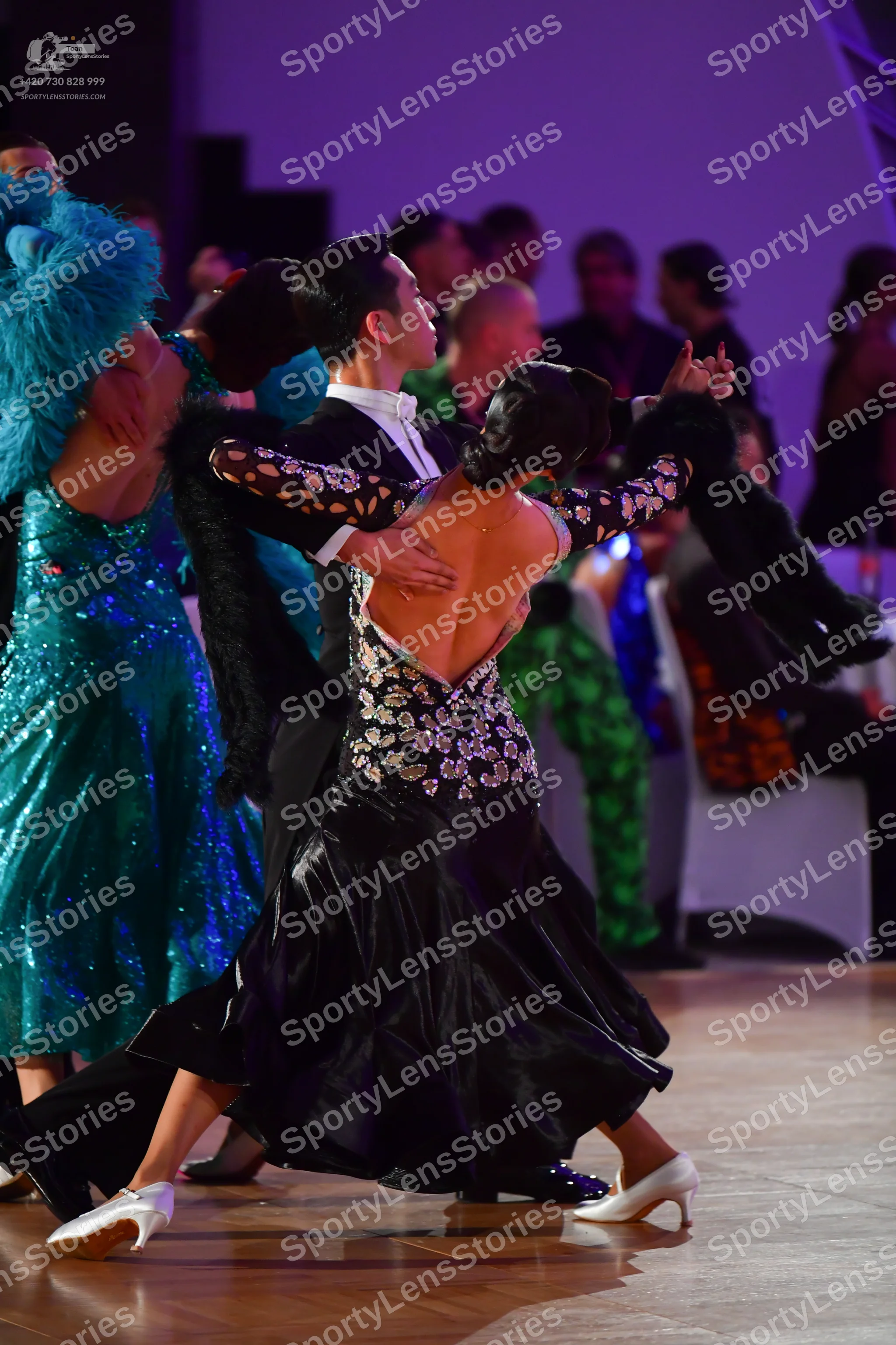 Dancesport competitor: Female dancer in foreground: black ballroom gown with a low back, a bodice embel