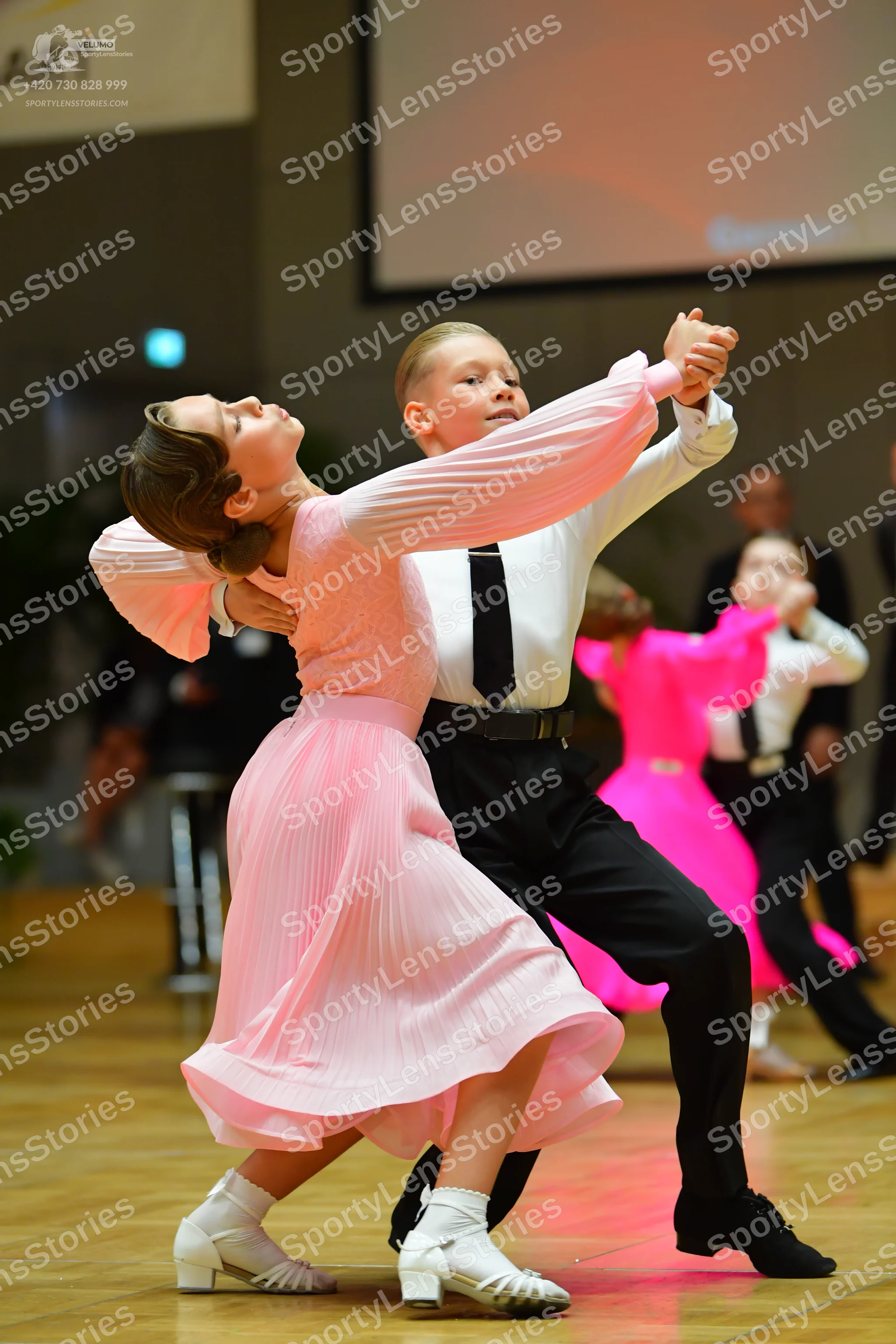 Dancesport competitor: Female dancer in foreground: light pink long-sleeved pleated dress