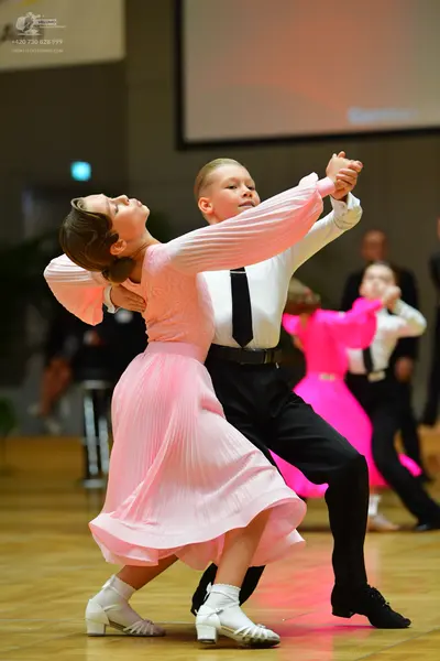 Dancesport competitor: Female dancer in foreground: light pink long-sleeved pleated dress