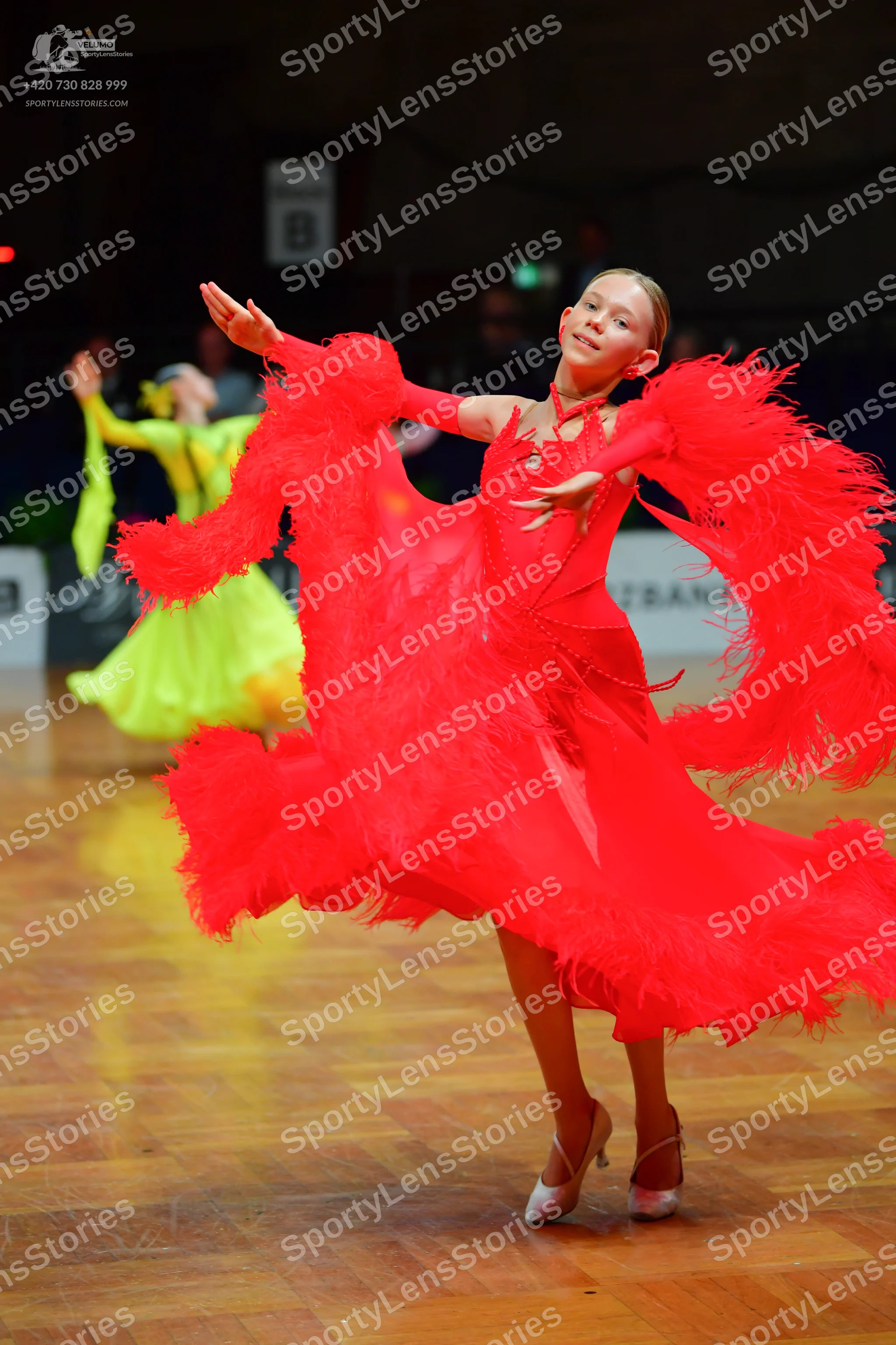 Dancesport competitor: Female dancer in foreground: bright red latin dance dress with voluminous, feath