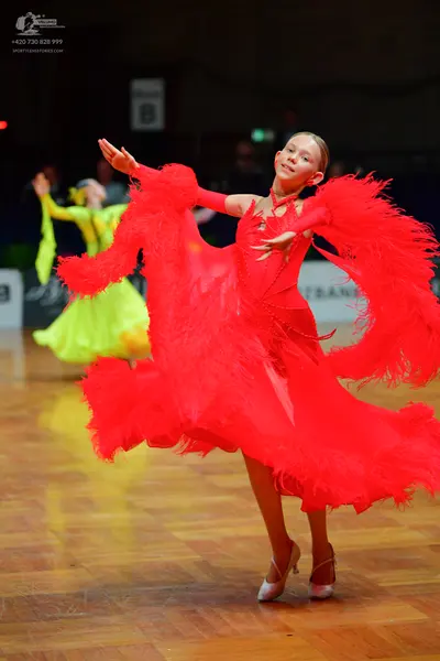 Dancesport competitor: Female dancer in foreground: bright red latin dance dress with voluminous, feath