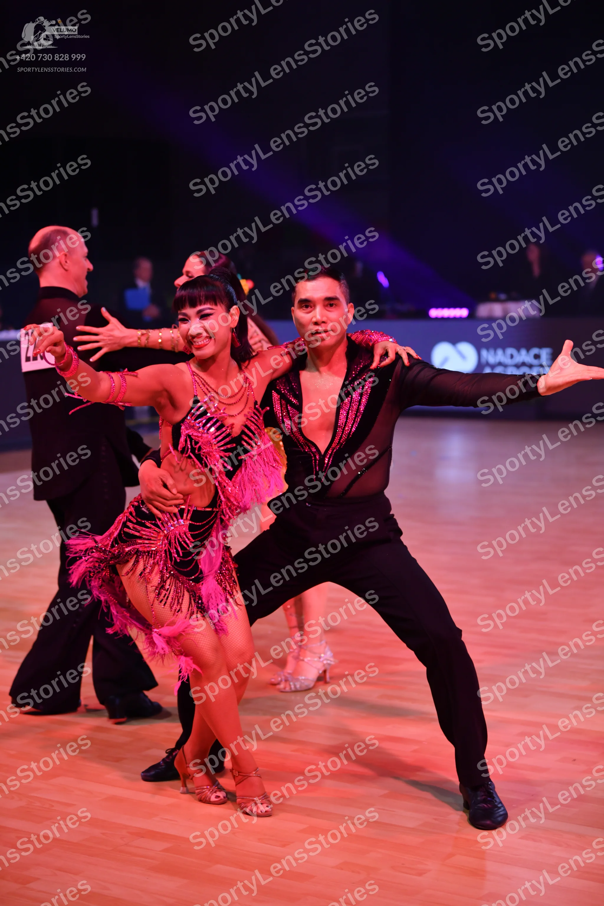 Dancesport competitor: Male dancer in foreground: black long-sleeved top with sheer mesh and sequins, b