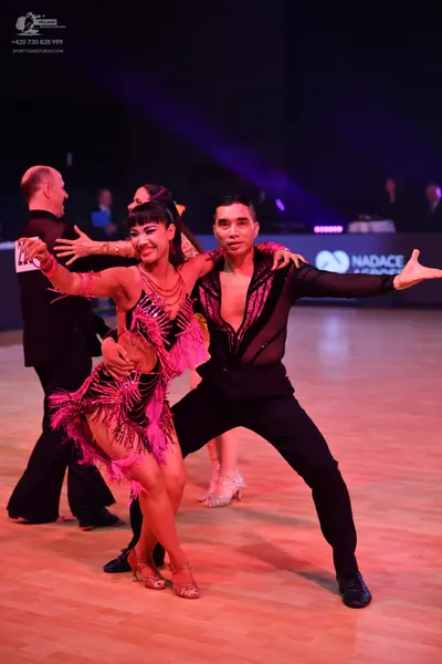 Dancesport competitor: Male dancer in foreground: black long-sleeved top with sheer mesh and sequins, b