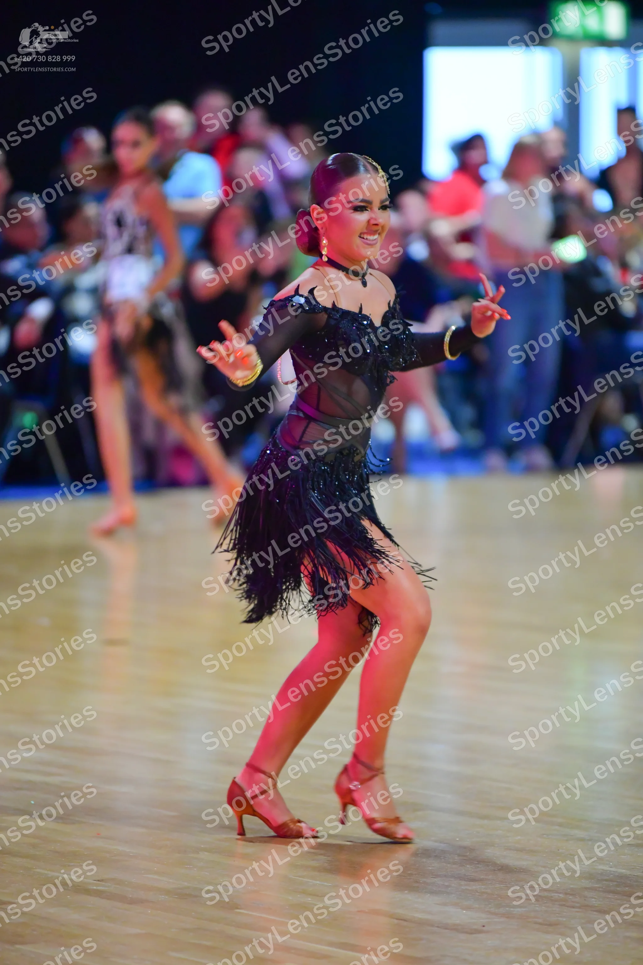 Dancesport competitor: Female dancer in foreground: black Latin dress with a sheer mesh bodice, black s