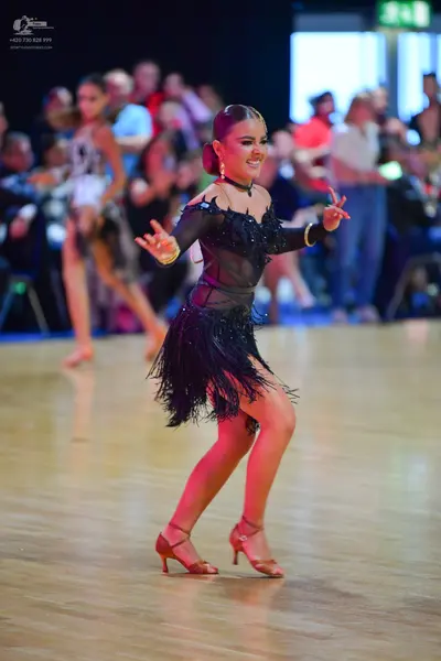 Dancesport competitor: Female dancer in foreground: black Latin dress with a sheer mesh bodice, black s