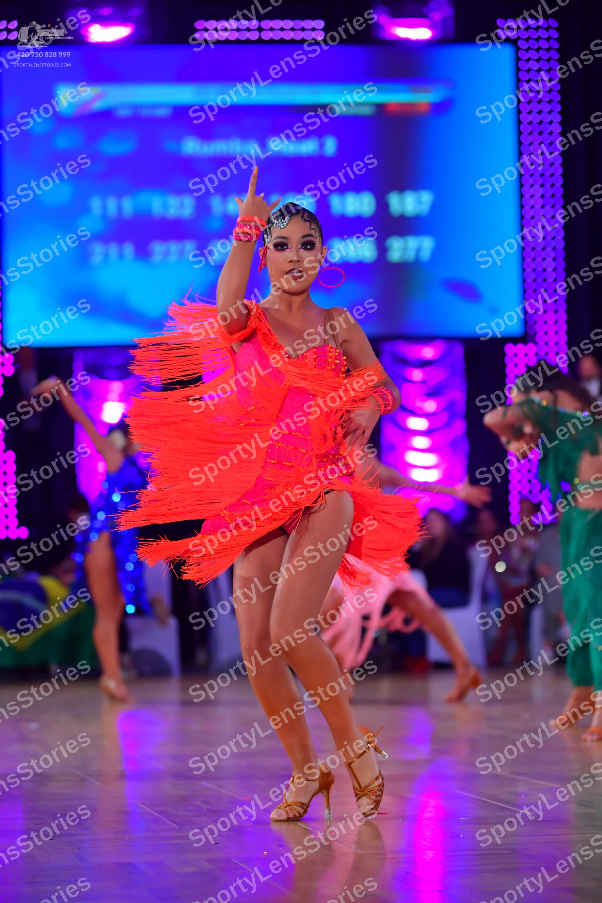 Dancesport competitor: Main dancer: bright orange Latin dress with heavy fringe and straps, wearing lar