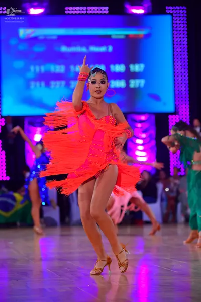 Dancesport competitor: Main dancer: bright orange Latin dress with heavy fringe and straps, wearing lar