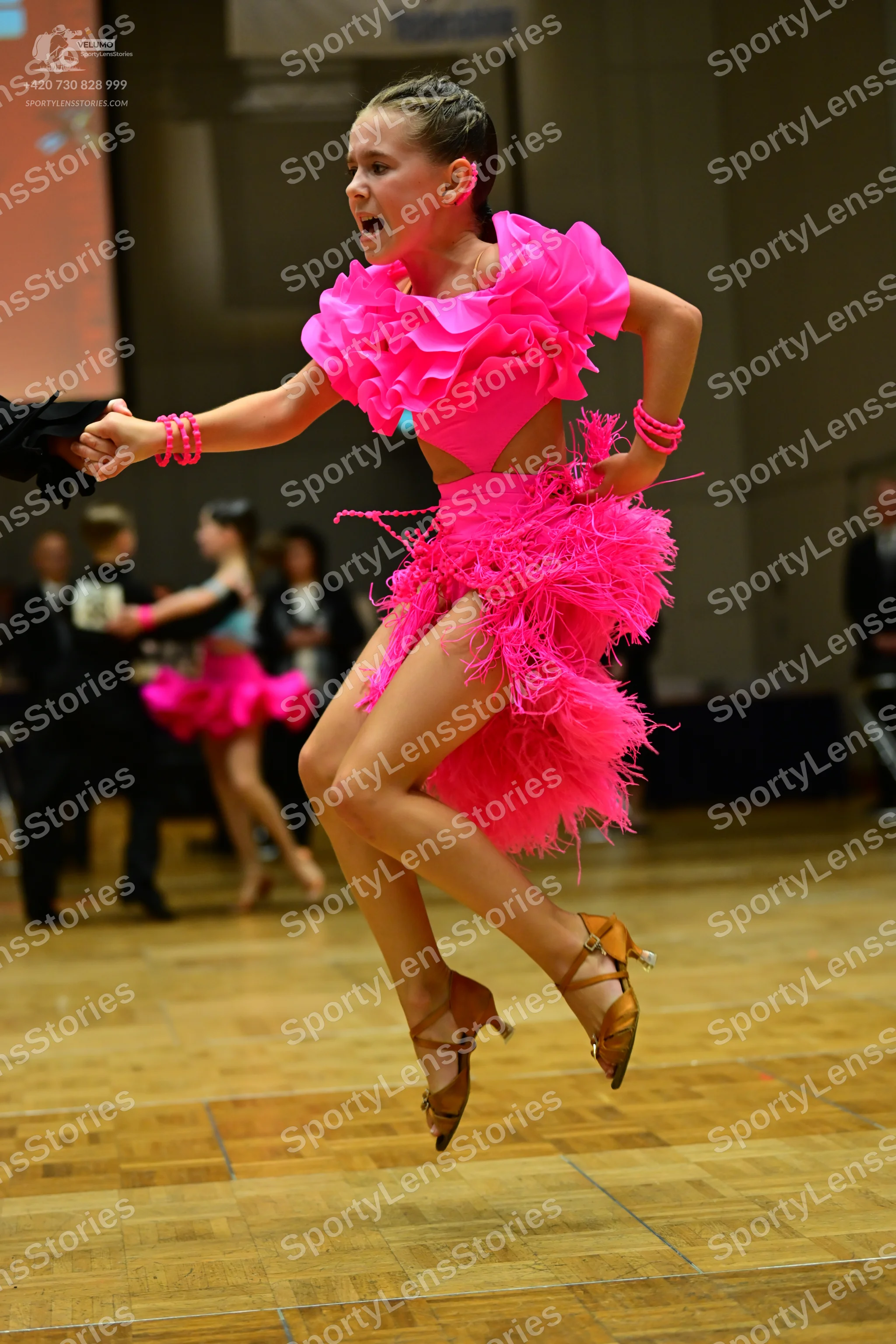 Dancesport competitor: Female dancer in foreground: bright pink Latin dance dress with a ruffled bodice