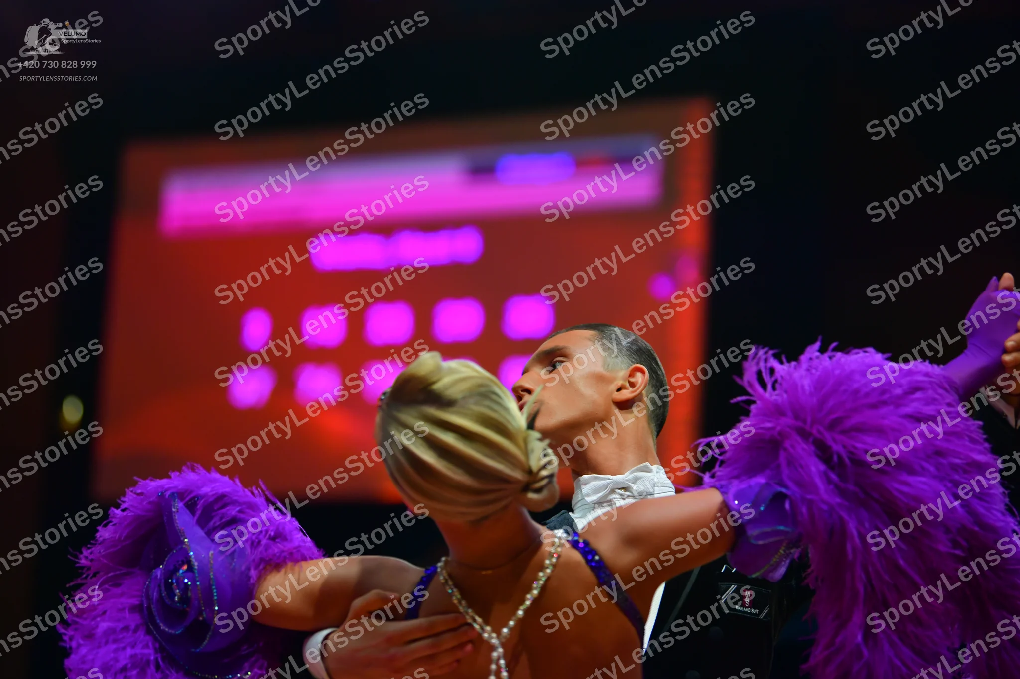 Dancesport competitor: Female dancer: purple Latin dance costume with large feather accents on the arms