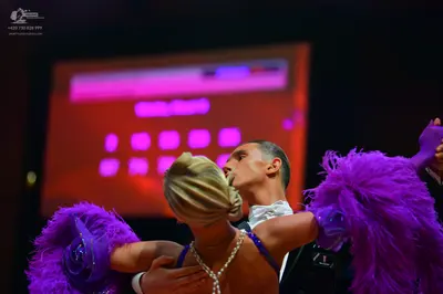 Dancesport competitor: Female dancer: purple Latin dance costume with large feather accents on the arms