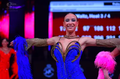 Dancesport competitor: Female dancer in foreground: blue Latin dance dress with gold sequined swirling 