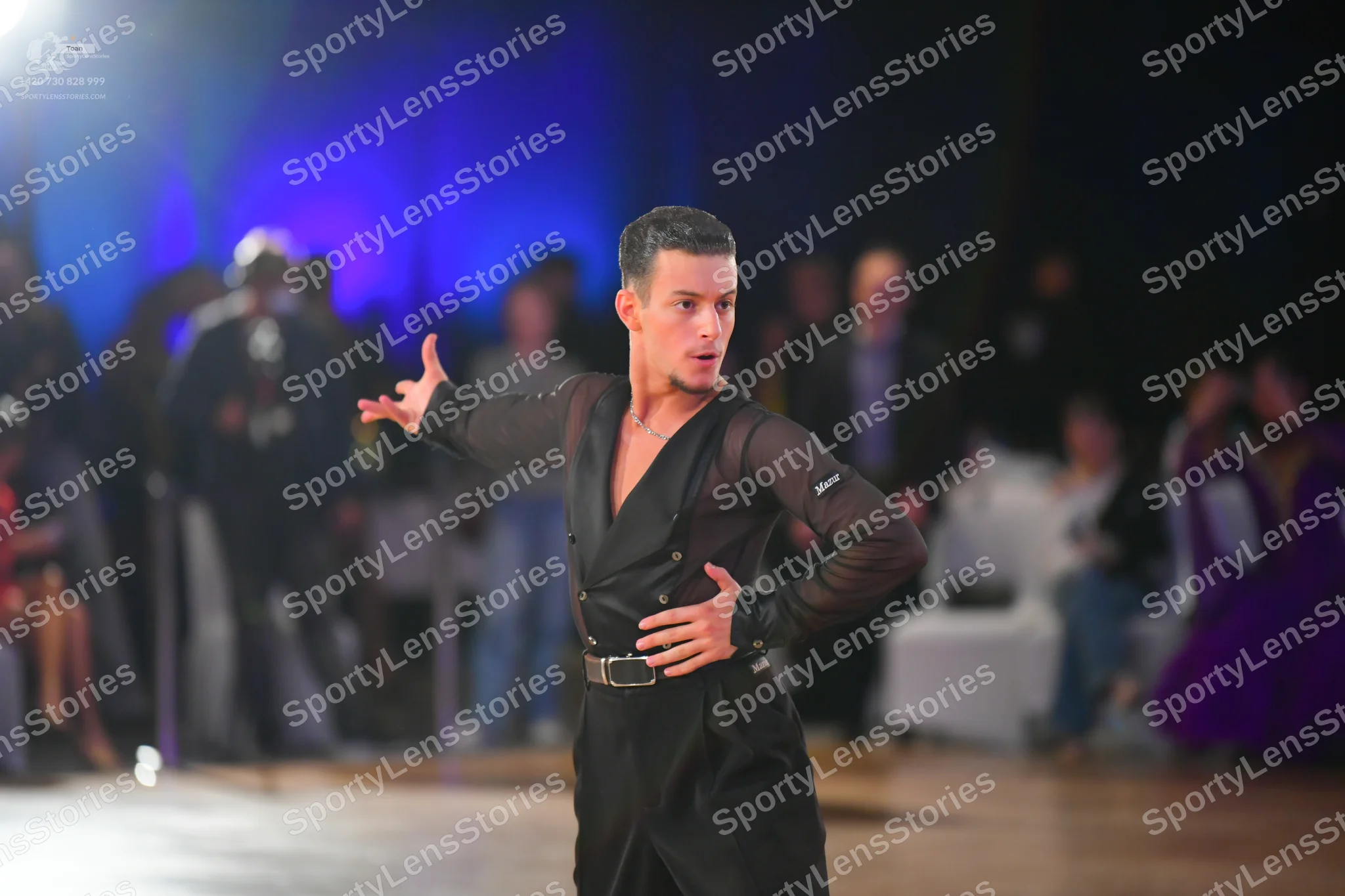 Dancesport competitor: Male dancer: black latin costume with semi-sheer/mesh sleeves, a black opaque to