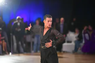 Dancesport competitor: Male dancer: black latin costume with semi-sheer/mesh sleeves, a black opaque to
