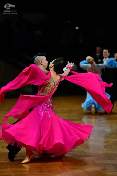 Dancesport competitor: Female dancer in foreground: bright pink ballroom dress with long, flowing sleev