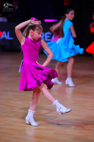 Dancesport competitor: Female dancer: magenta sleeveless dress with a ruffled skirt, white ruffled sock