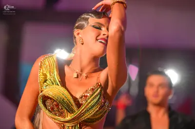 Dancesport competitor: Female dancer: gold and yellow sequined Latin dress with a draped design, wearin