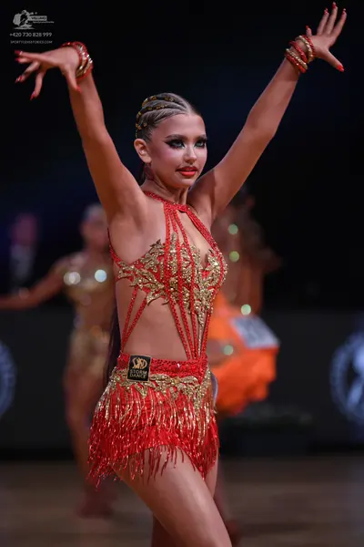 Dancesport competitor: Female dancer in foreground: red Latin dress with gold/bronze sequin/beaded patt