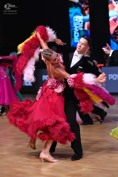 Dancesport competitor: Female dancer: pink Latin dress with large pink, white, and yellow feathered/fri