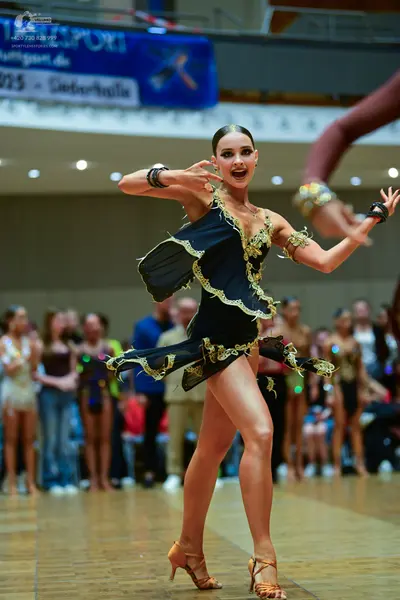 Dancesport competitor: Female dancer: black latin dress with gold sequin trim and ruffled skirt