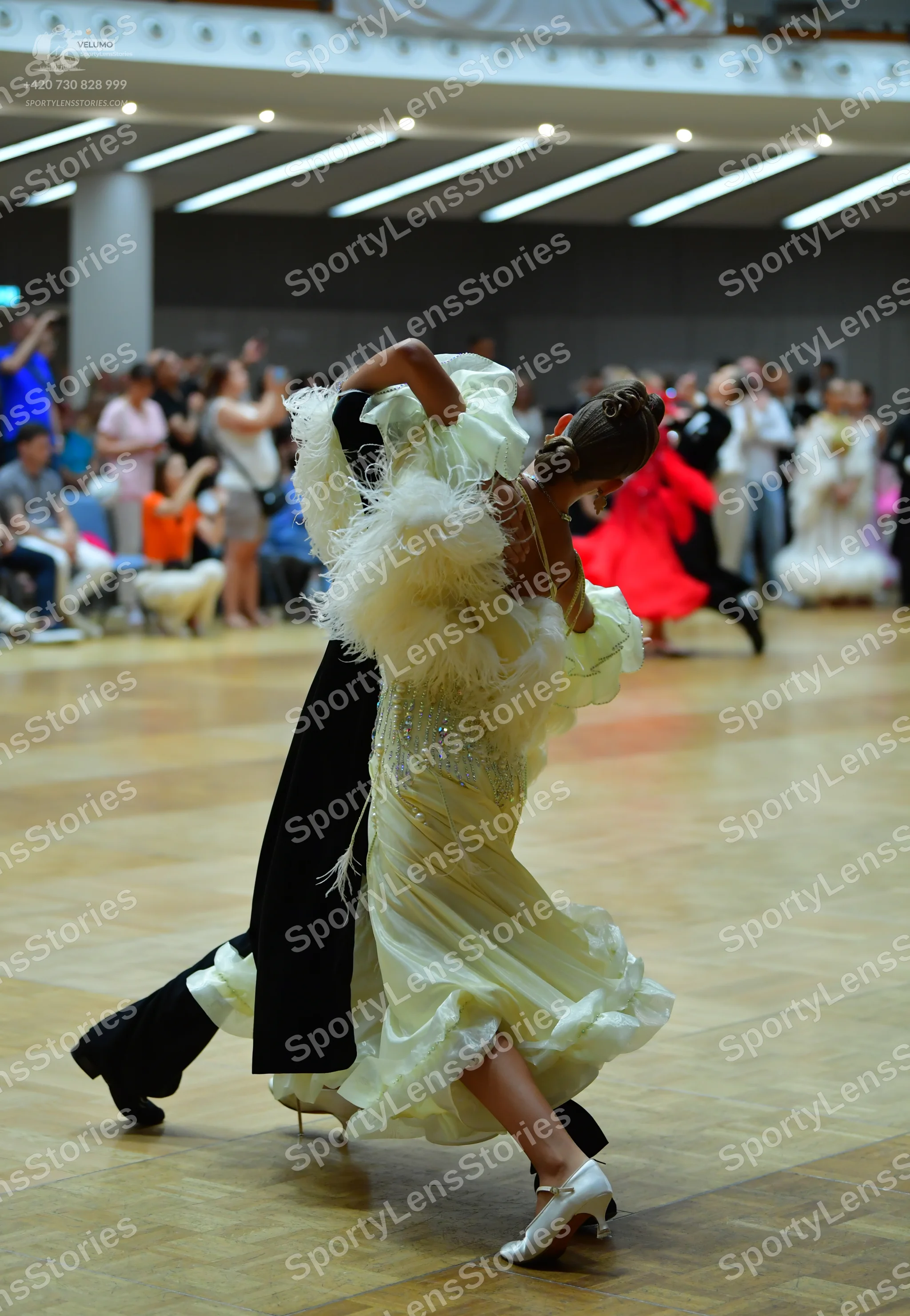 Dancesport competitor: Female dancer in foreground: voluminous, pale yellow/cream-colored ballgown with