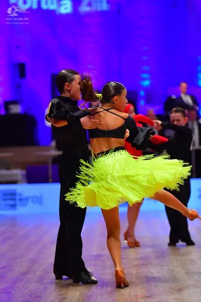 Dancesport competitor: Female dancer in foreground: black crop top and bright yellow fringe skirt