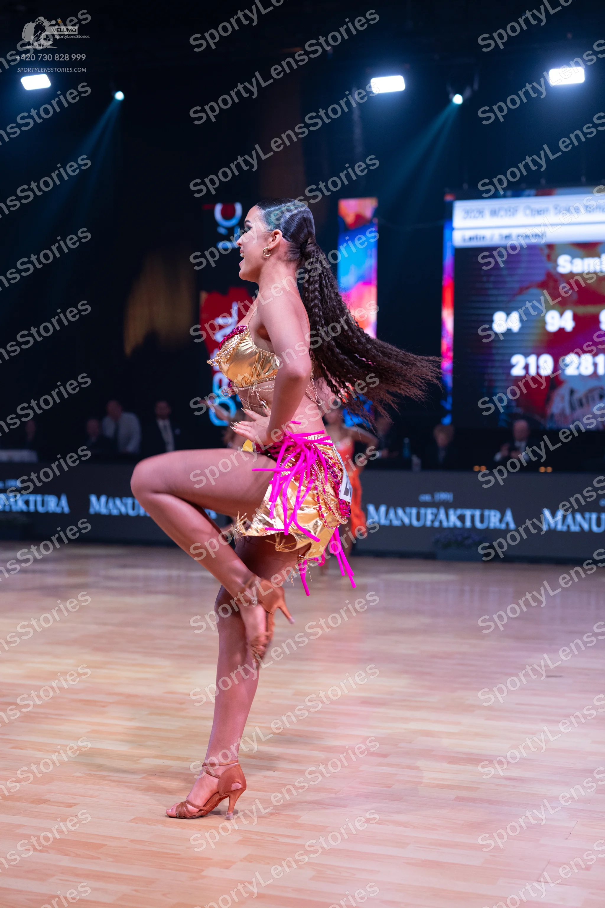 Dancesport competitor: Female dancer: gold sequined top and a gold skirt with long, bright pink fringes
