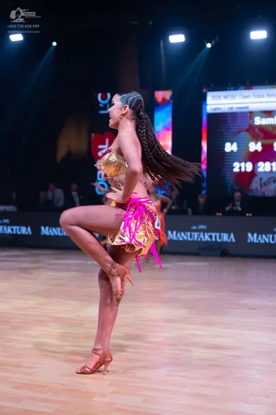 Dancesport competitor: Female dancer: gold sequined top and a gold skirt with long, bright pink fringes