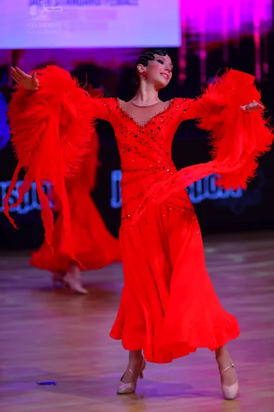 Dancesport competitor: Female dancer: red latin dress with sequined bodice and large feathered sleeves