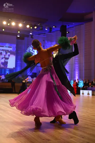 Dancesport competitor: Female dancer: pink flowing ballroom gown with a pleated skirt and dark green fe