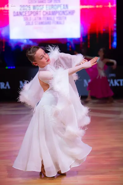 Dancesport competitor: Female dancer in foreground: white ballroom gown with white feather-like trim